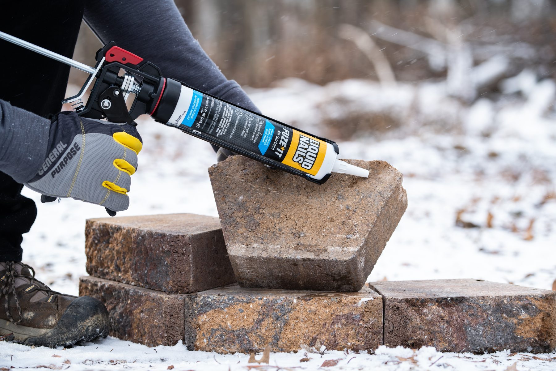 Gloved hand applying Liquid Nails Fuze*It to a landscape block in the snow